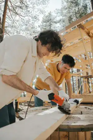 Deux hommes font des travaux en extérieur, l'un d'eux manipule une scie circulaire et l'autre une meuleuse d'angle